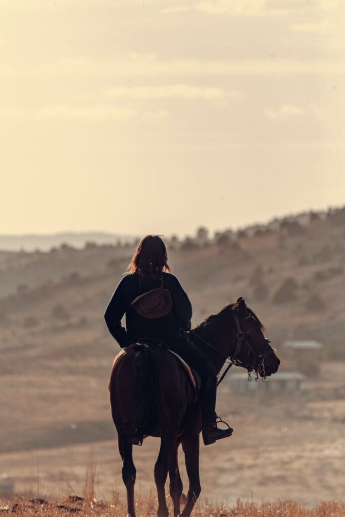 A young woman rides a horse across the rural landscape of Konya at sunset, enjoying nature and serenity.