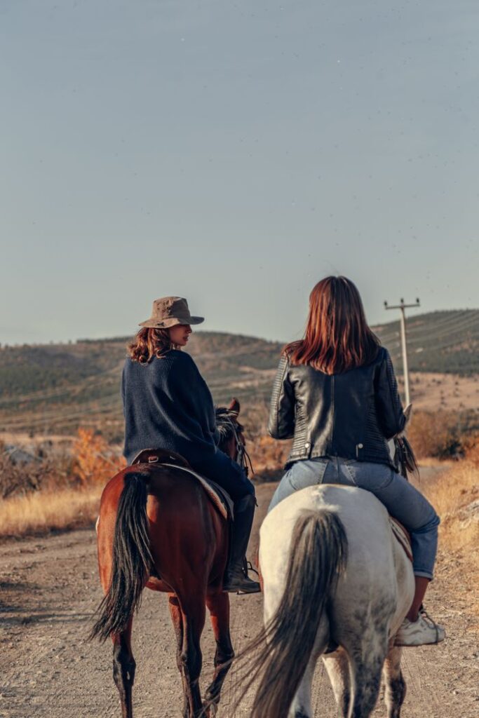 Two women riding horses on a rural dirt road in the scenic landscapes of Konya, Türkiye.