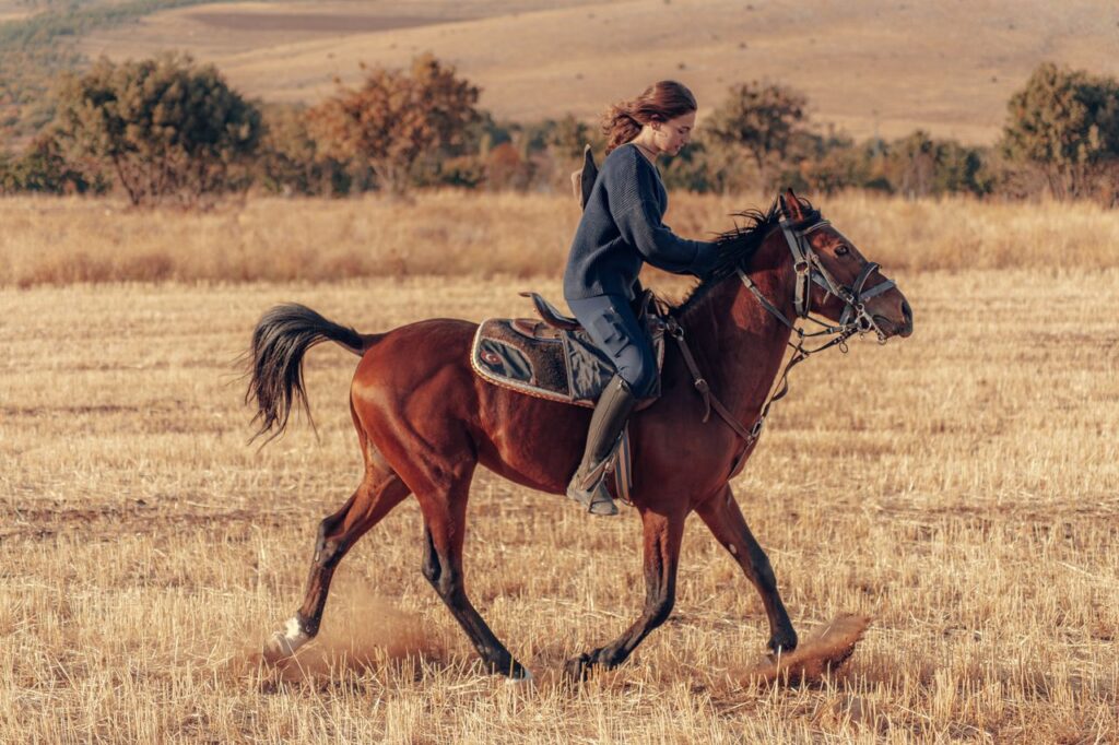 A young woman enjoying horseback riding on a brown horse in a rural field in Konya, Türkiye.