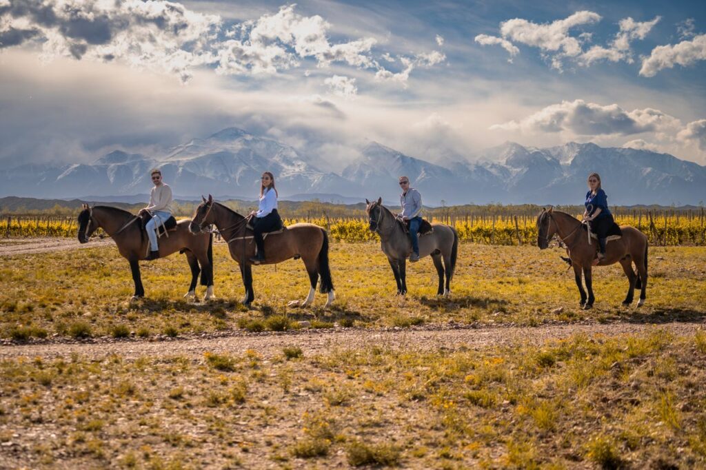 Four people horse riding in a beautiful mountain landscape under a vibrant sky.